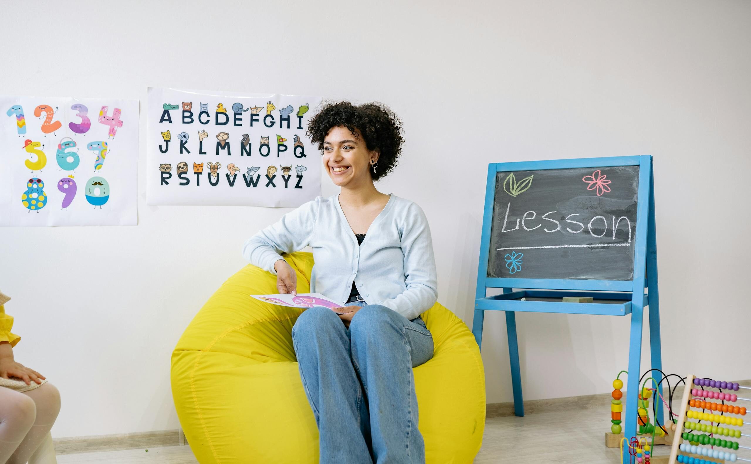 Smiling teacher sitting in a classroom, holding a book and teaching preschool students.